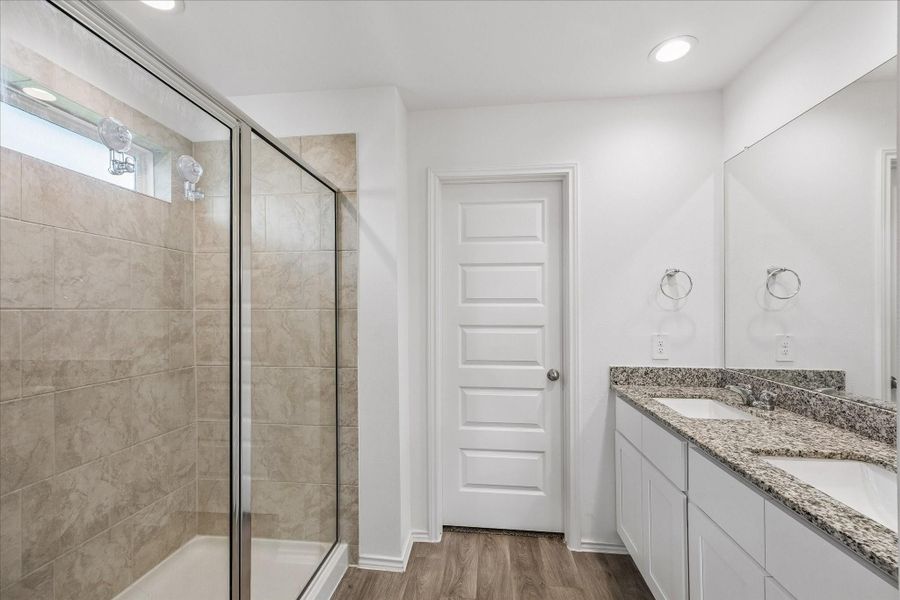 Primary bathroom with a spacious glass-enclosed shower. Recessed lighting and wood-look flooring, creating a clean and elegant feel.
