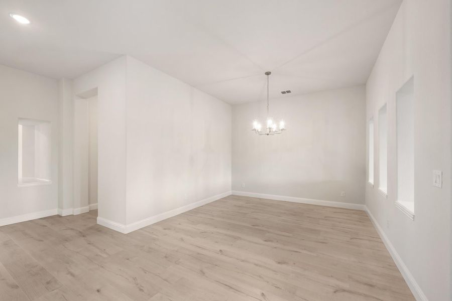 Empty dining room with light wood floors, white walls, and a chandelier overhead