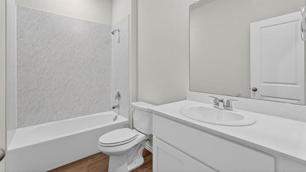 Bathroom featuring a white vanity with an undermount sink, a large mirror, a white toilet, a white bathtub, and a shower with textured wall panels Bathroom featuring a white vanity with an undermount sink, a large mirror, a white toilet, a white bathtub, and a shower with textured wall panels