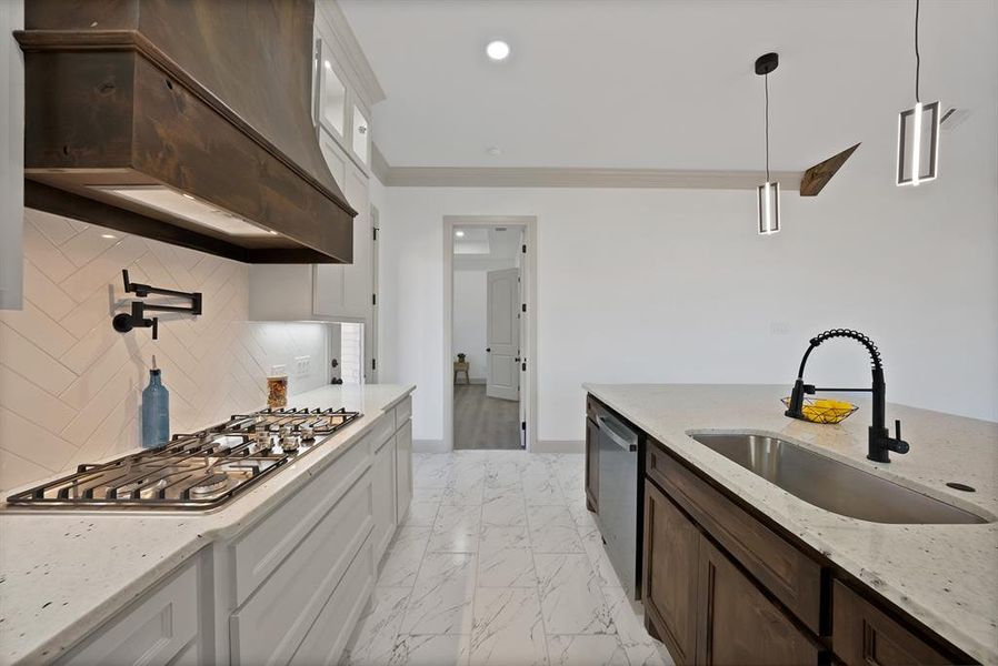 Kitchen featuring light stone countertops, custom range hood, light marble finish flooring, decorative light fixtures, and stainless steel appliances