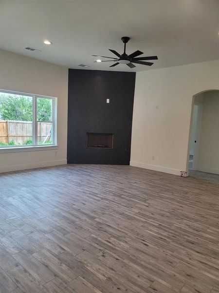 Unfurnished living room featuring a ceiling fan, arched walkways, wood finished floors, recessed lighting, and a fireplace