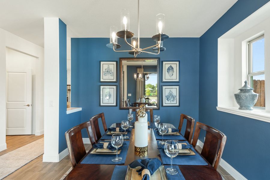 Formal dining room with blue accent walls, wood table set for six, and modern chandelier overhead