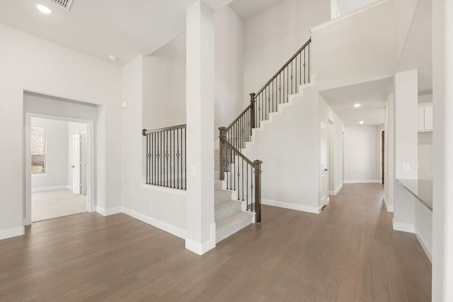 Open foyer with two-story ceiling, staircase with iron balusters, and hardwood floors