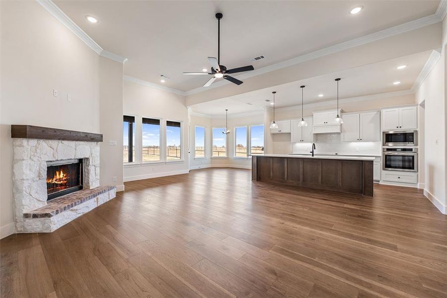 Unfurnished living room featuring a stone fireplace, a ceiling fan, dark wood-style flooring, recessed lighting, and ornamental molding