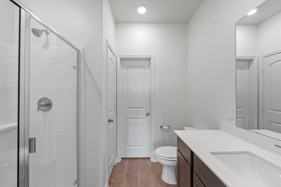 Bathroom with vanity, toilet, an enclosed shower, and wood-style flooring