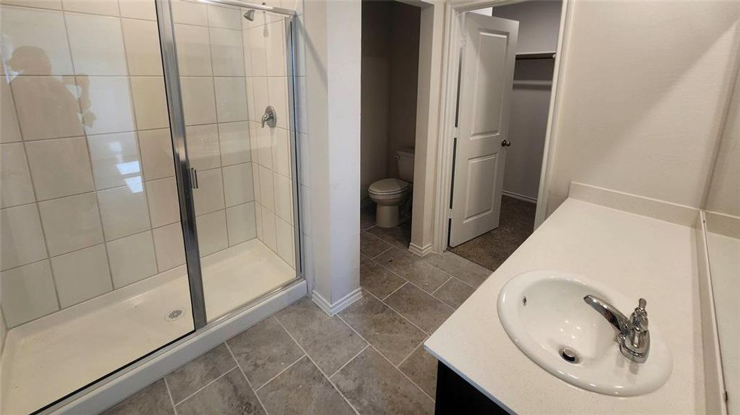 Bathroom featuring a glass-enclosed shower with white tiled walls, a single-basin vanity with a white countertop and chrome faucet, and large format floor tiling