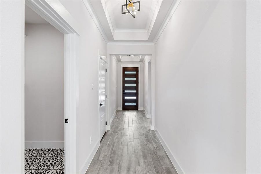 Corridor with light hardwood / wood-style flooring, ornamental molding, and a tray ceiling