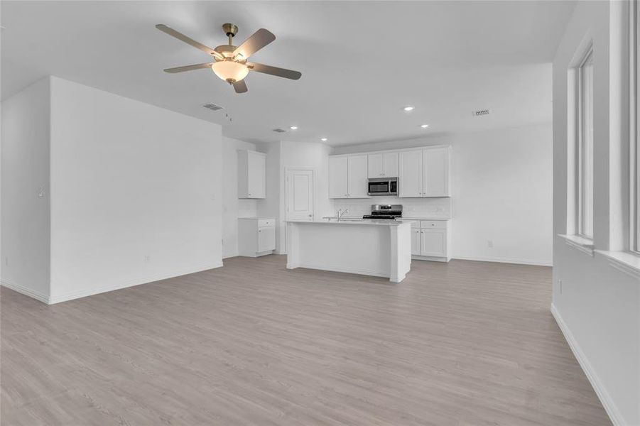 Kitchen featuring light wood-type flooring, white cabinets, stainless steel appliances, a center island with sink, and ceiling fan