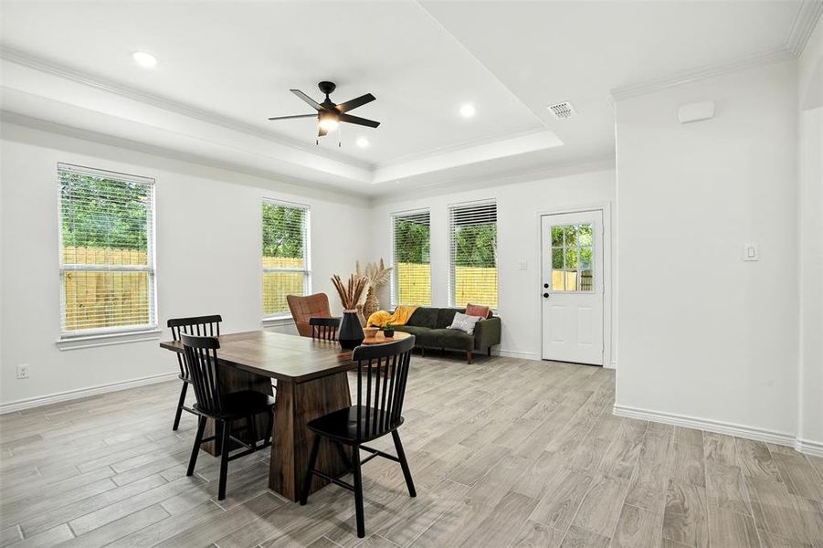 Dining space with ornamental molding, light wood finished floors, a tray ceiling, a ceiling fan, and recessed lighting