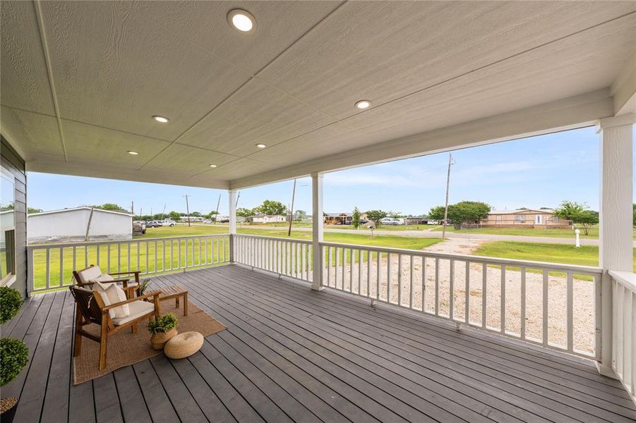 Expansive covered porch featuring grey wood-finish decking, recessed lighting, white railing, and structural support columns