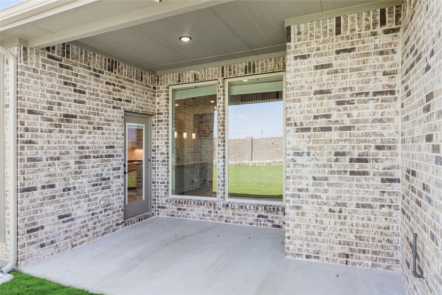 Covered back patio with concrete floor, brick exterior, sliding glass door, and view of fenced backyard