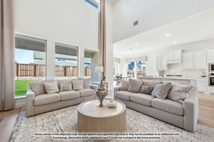 Open living room with two-story ceiling, two beige sofas, and open kitchen visible in background Open living room with two-story ceiling, two beige sofas, and open kitchen visible in background