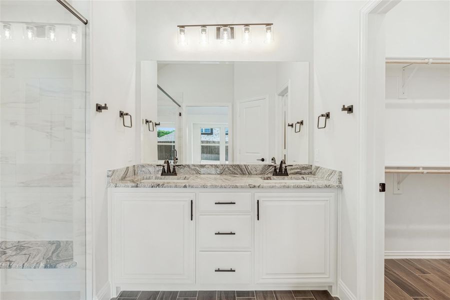 Bathroom with double sink vanity, white cabinets, granite countertop, large mirror, and glass shower door nearby. Bathroom with double sink vanity, white cabinets, granite countertop, large mirror, and glass shower door nearby.