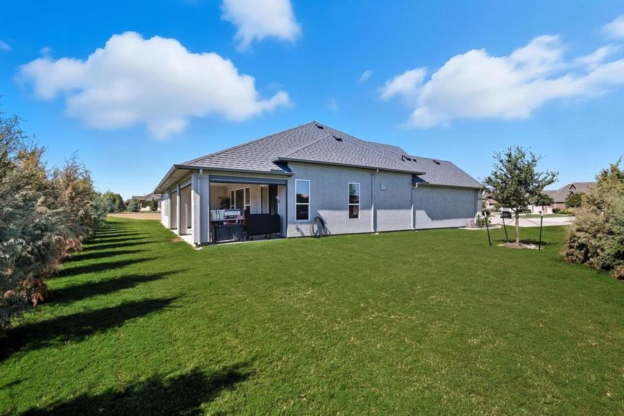 Expansive green lawn with a covered patio, multiple windows, and a mature tree