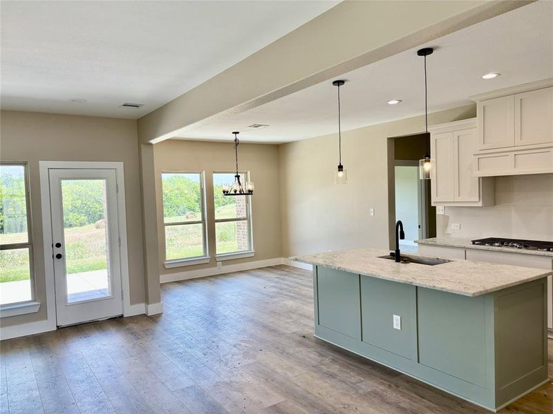 Kitchen featuring a center island with sink, stainless steel gas stovetop, light stone counters, light wood finished floors, and white cabinets Kitchen featuring a center island with sink, stainless steel gas stovetop, light stone counters, light wood finished floors, and white cabinets