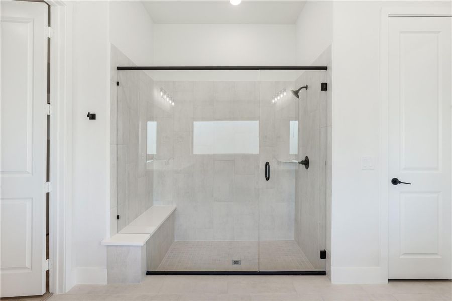 Walk-in shower with glass doors, gray tile walls, built-in bench, and matte black fixtures