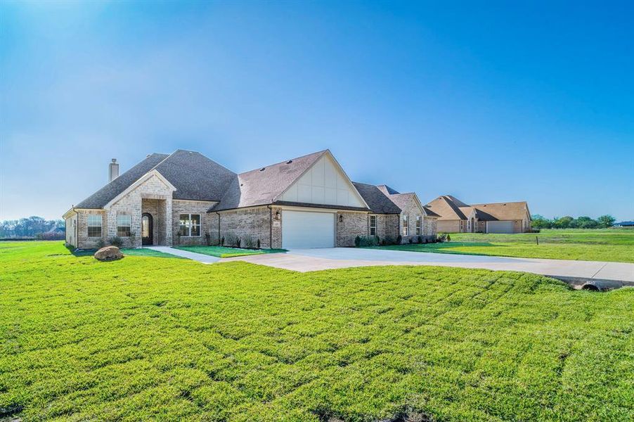 French provincial home featuring concrete driveway, a front yard, brick siding, and a chimney