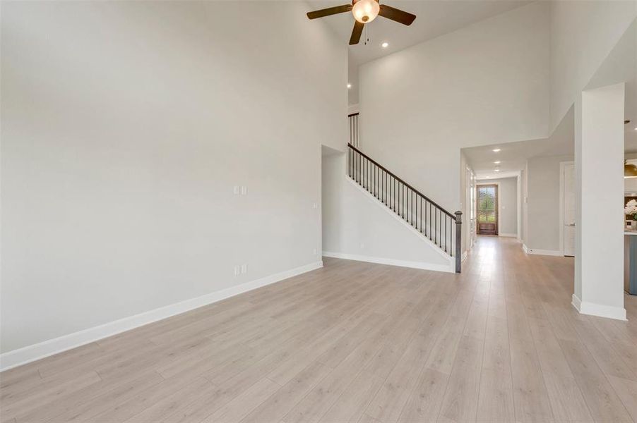 Spacious interior featuring a vaulted ceiling, wood-finish flooring, recessed lighting, and a prominent staircase with dark wood railings