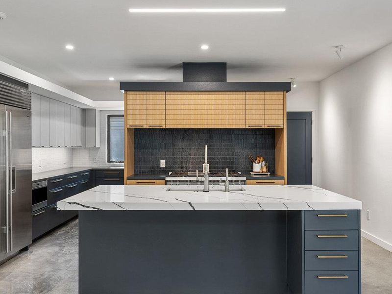 Kitchen featuring a kitchen island with sink, modern cabinets, built in fridge, light stone counters, and recessed lighting