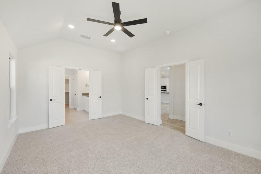 Empty bedroom with carpet, ceiling fan, and open doors leading to bathroom and closet Empty bedroom with carpet, ceiling fan, and open doors leading to bathroom and closet