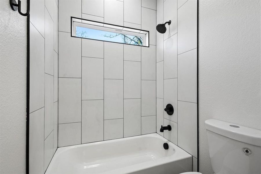 Bathroom featuring tiled shower / bath combo and toilet