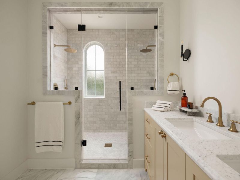 Marble finishes elevate this modern primary bathroom with dual shower heads and a spacious vanity.