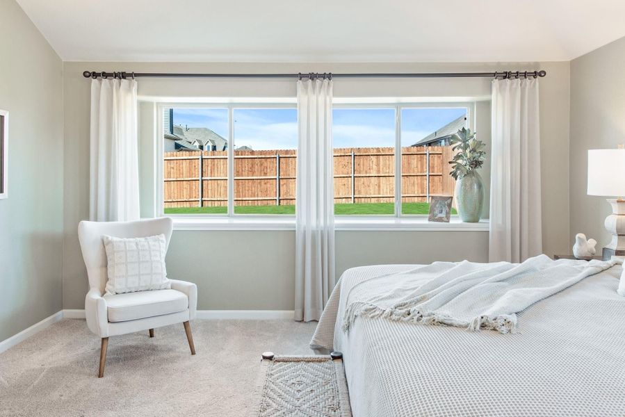 Bedroom with large window, white curtains, accent chair, and neutral carpet flooring Bedroom with large window, white curtains, accent chair, and neutral carpet flooring