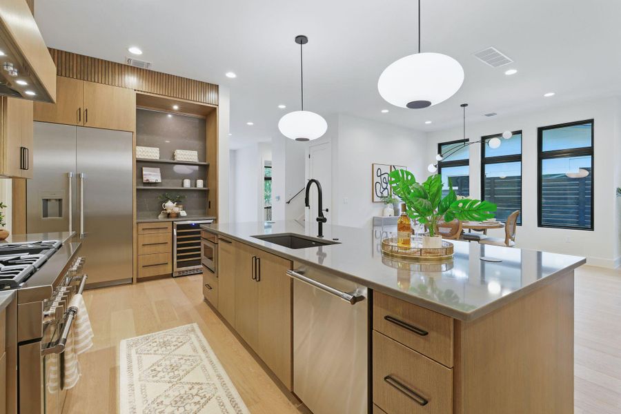 Kitchen featuring wine cooler, high end appliances, custom range hood, light wood finished floors, and a center island with sink