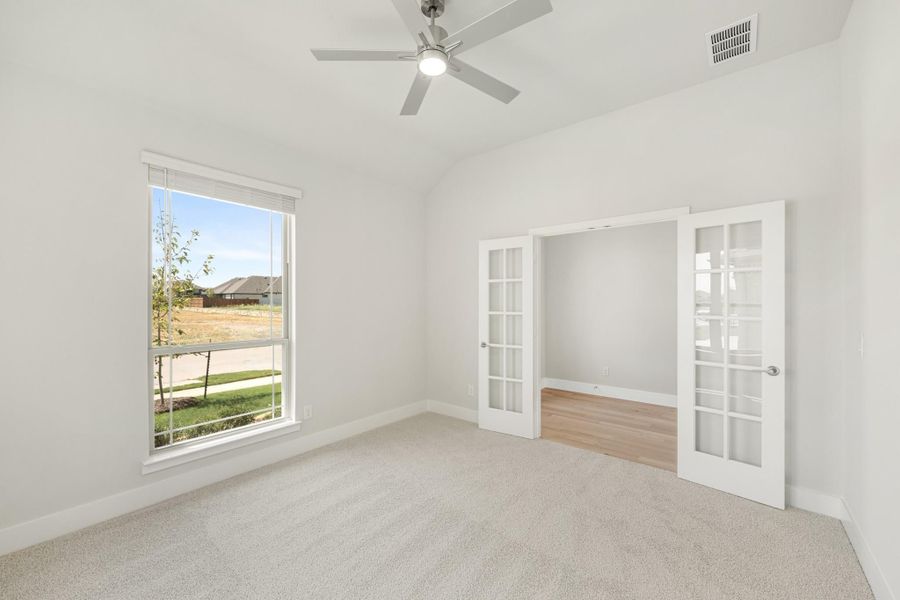 Empty bedroom with vaulted ceiling, ceiling fan, carpet, large window, and French doors leading to an adjoining room