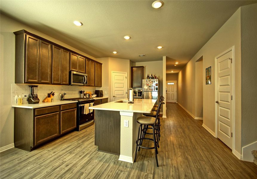 Kitchen featuring stainless steel appliances, dark wood finish cabinets, a kitchen island with sink, light stone counters, and a kitchen breakfast bar Kitchen featuring stainless steel appliances, dark wood finish cabinets, a kitchen island with sink, light stone counters, and a kitchen breakfast bar