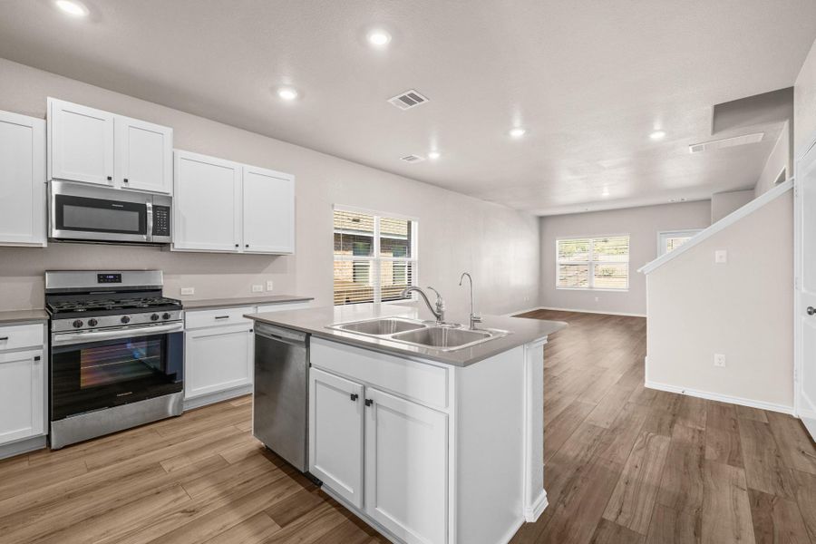 Kitchen with stainless steel appliances, a kitchen island with sink, white cabinets, recessed lighting, and light wood finished floors