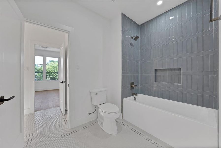Bathroom featuring a white soaking tub with matte black fixtures, gray subway tile surround with an integrated niche, and white hex mosaic floor tile