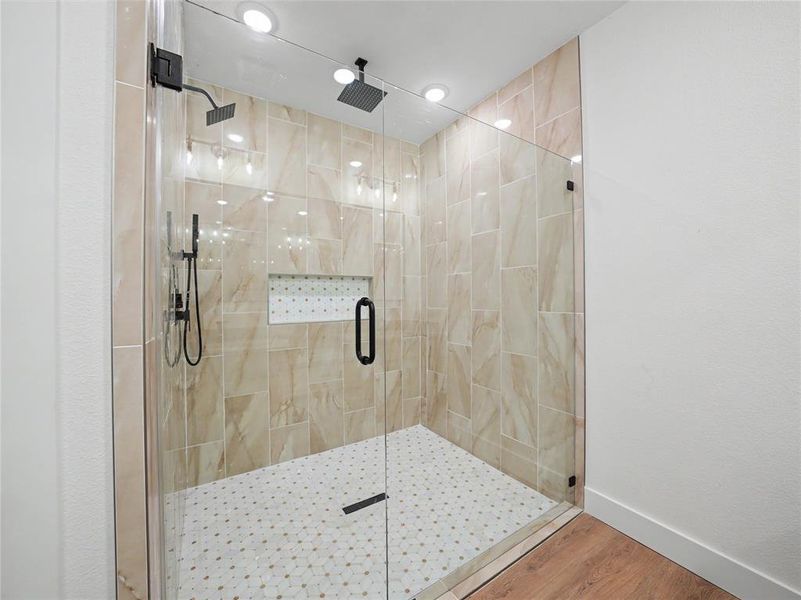 Glass-enclosed shower featuring floor-to-ceiling beige tile, a built-in tiled niche, and dual matte black showerheads Glass-enclosed shower featuring floor-to-ceiling beige tile, a built-in tiled niche, and dual matte black showerheads