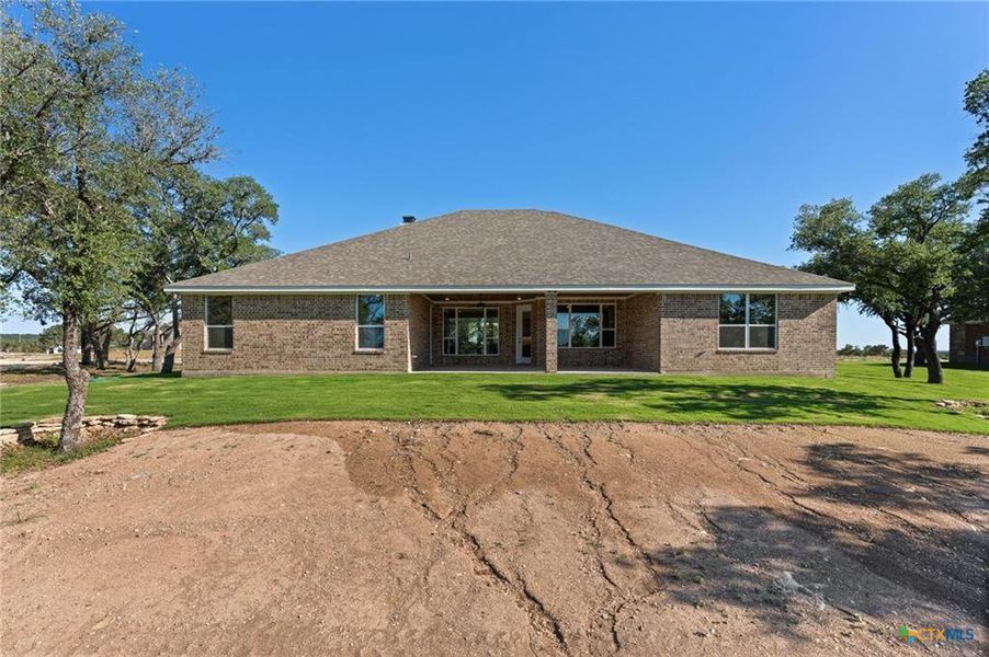Back of property featuring brick siding, a patio area, and a lawn