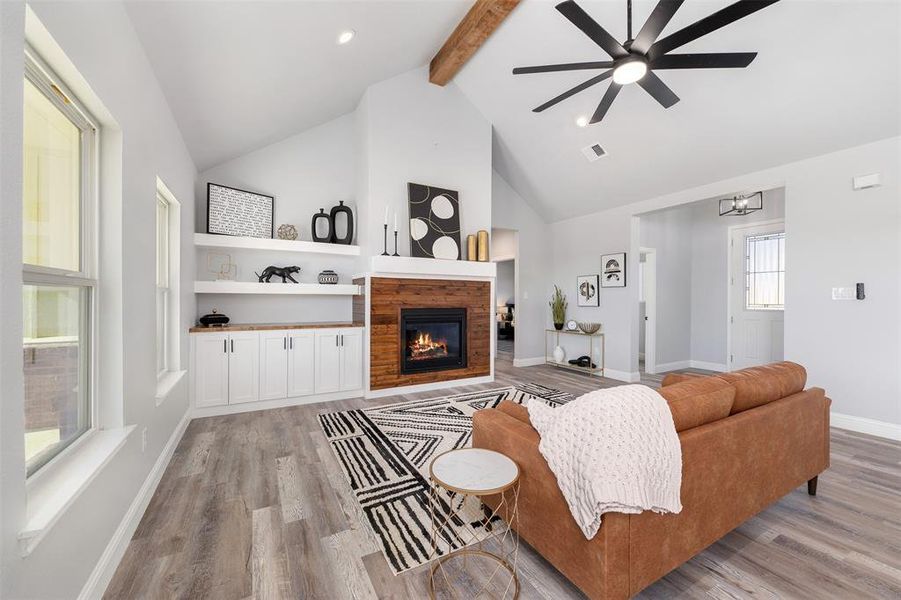 Living room with ceiling fan, light wood-type flooring, a tile fireplace, and vaulted ceiling with beams