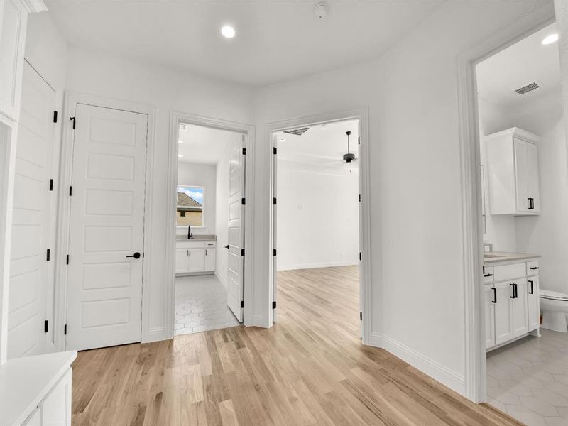 Corridor featuring visible vents, baseboards, a sink, light wood-style floors, and recessed lighting Corridor featuring visible vents, baseboards, a sink, light wood-style floors, and recessed lighting
