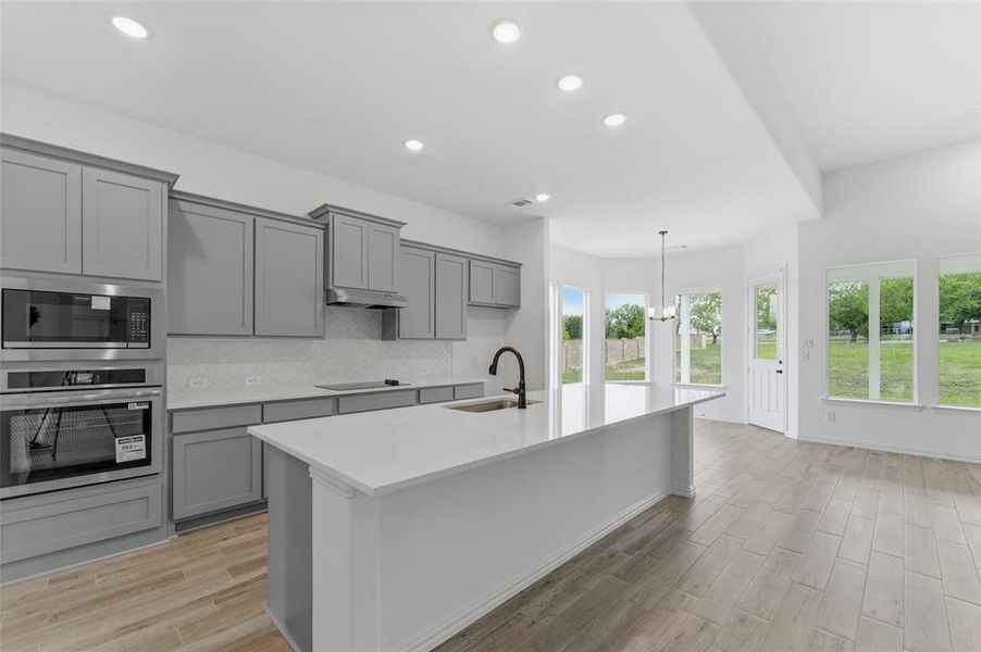 Contemporary kitchen featuring gray cabinetry, stainless steel appliances, a white island with a sink and a dark faucet, and light wood-style flooring