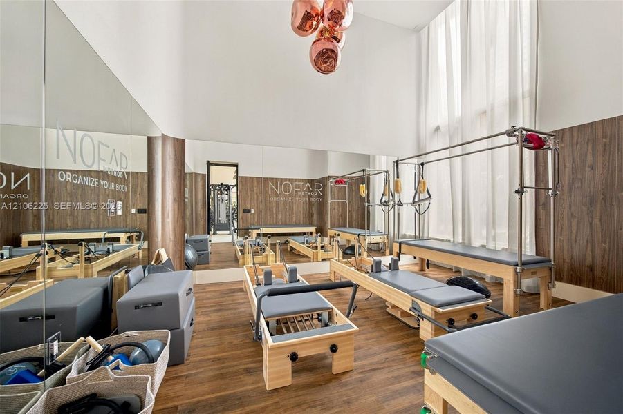 Double-height ceilings, floor-to-ceiling mirror wall, wood-finish wall paneling, wood-finish flooring, and multi-globe pendant light fixture Double-height ceilings, floor-to-ceiling mirror wall, wood-finish wall paneling, wood-finish flooring, and multi-globe pendant light fixture