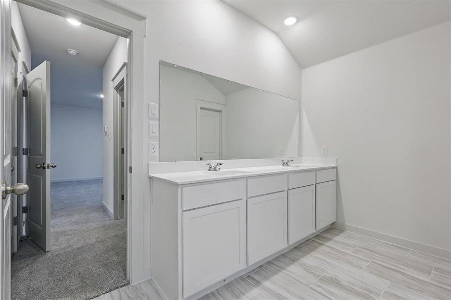 Bathroom with double vanity, vaulted ceiling, baseboards, and a sink Bathroom with double vanity, vaulted ceiling, baseboards, and a sink
