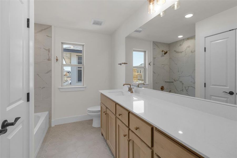 Bathroom featuring a light wood-finish vanity with a white countertop and dual sinks, complemented by a large mirror