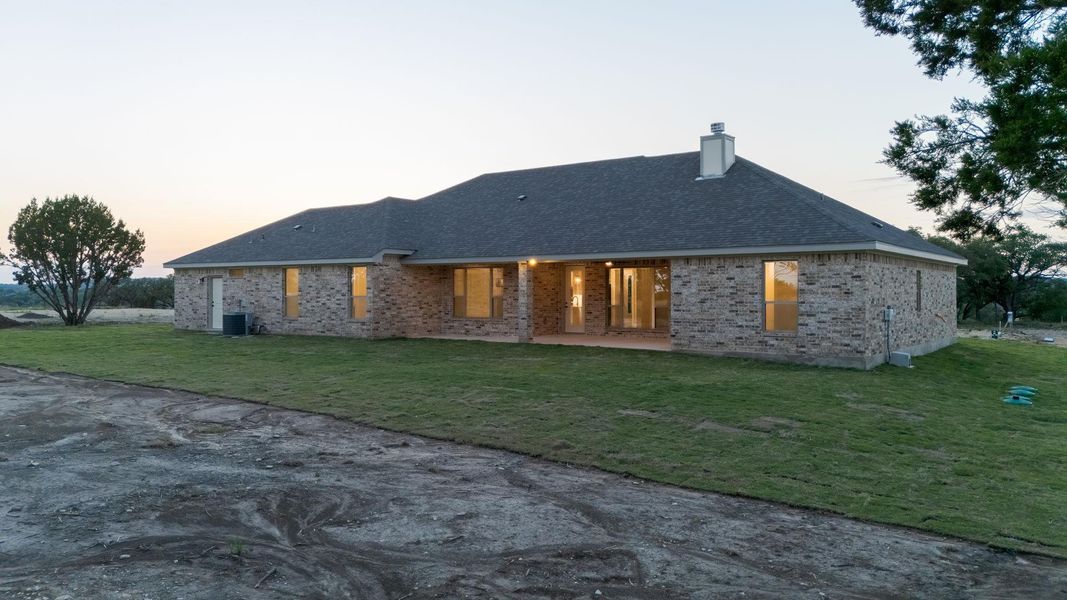 Back of house at dusk with a lawn, a patio, brick siding, and a chimney Back of house at dusk with a lawn, a patio, brick siding, and a chimney