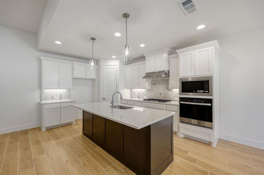 Kitchen with wood tiled floors, wall oven, backsplash, and two tone cabinetry