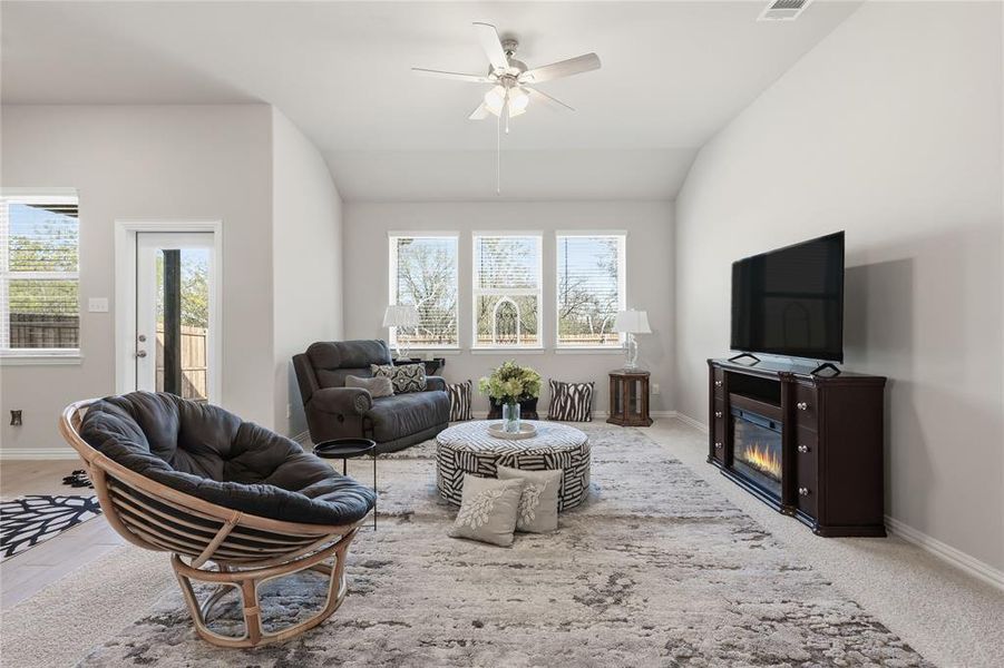 Carpeted living area featuring a vaulted ceiling with a ceiling fan, light gray walls, and multiple windows with blinds