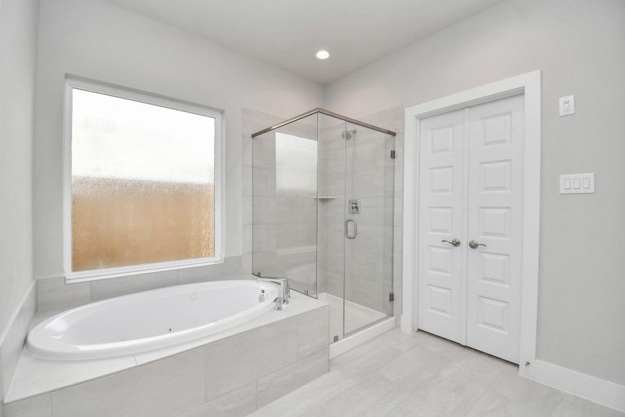 Indulge in a spa-like retreat within the confines of this primary bathroom. Delight in a spacious walk-in shower enveloped in stylish tile surround and unwind in a separate garden tub adorned with custom detailing. Sample photo of completed home with similar floor plan. Actual colors and selections may vary.
