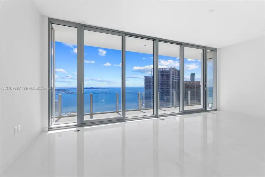 Floor-to-ceiling glass panel walls, expansive terrace with glass railing, large-format polished tile flooring, and panoramic water and city scenery