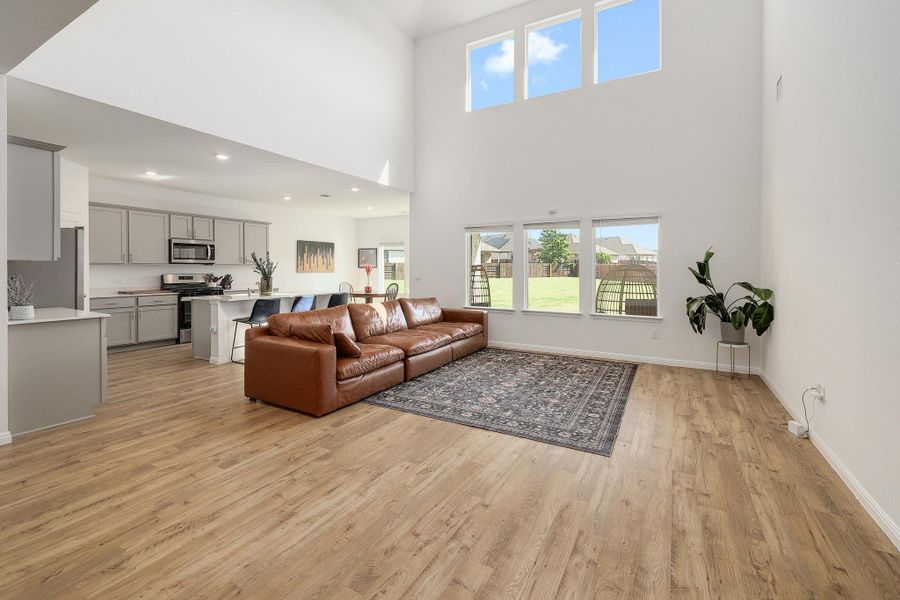 Spacious living area featuring wood-finish flooring, a two-story ceiling, and a bright interior from multiple windows Spacious living area featuring wood-finish flooring, a two-story ceiling, and a bright interior from multiple windows