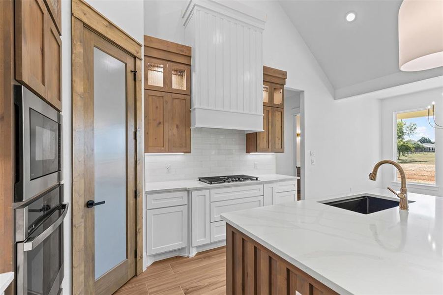 Kitchen featuring brown cabinets, glass insert cabinets, tasteful backsplash, wood tiled floors, and light stone counters