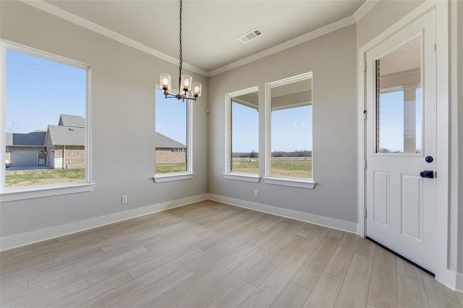 Unfurnished dining area with a chandelier, ornamental molding, light wood-type flooring, and healthy amount of natural light