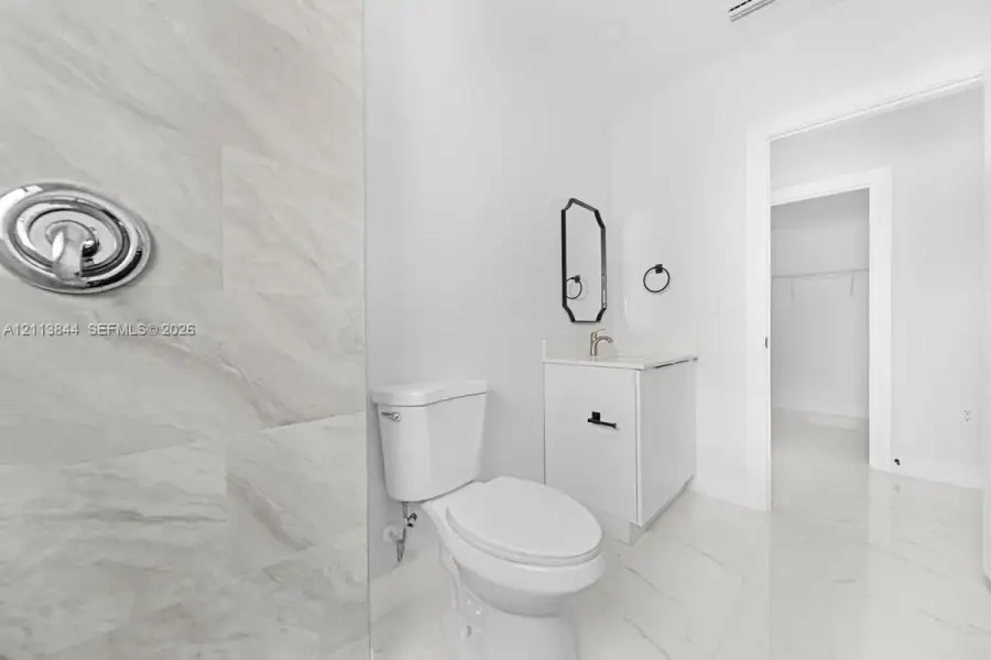 Bathroom featuring stone-finish wall tile, polished large-format floor tile, white vanity cabinet with a stone-surface countertop, and a wall-mounted decorative mirror Bathroom featuring stone-finish wall tile, polished large-format floor tile, white vanity cabinet with a stone-surface countertop, and a wall-mounted decorative mirror