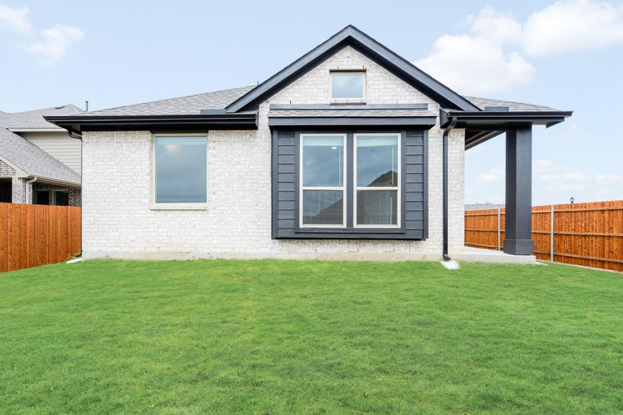 Rear exterior of single-story brick home with covered patio, large windows, and fenced backyard lawn